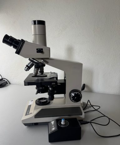 Mikroskop mit mehreren Objektiven auf einem Tisch, elektrisch betrieben.